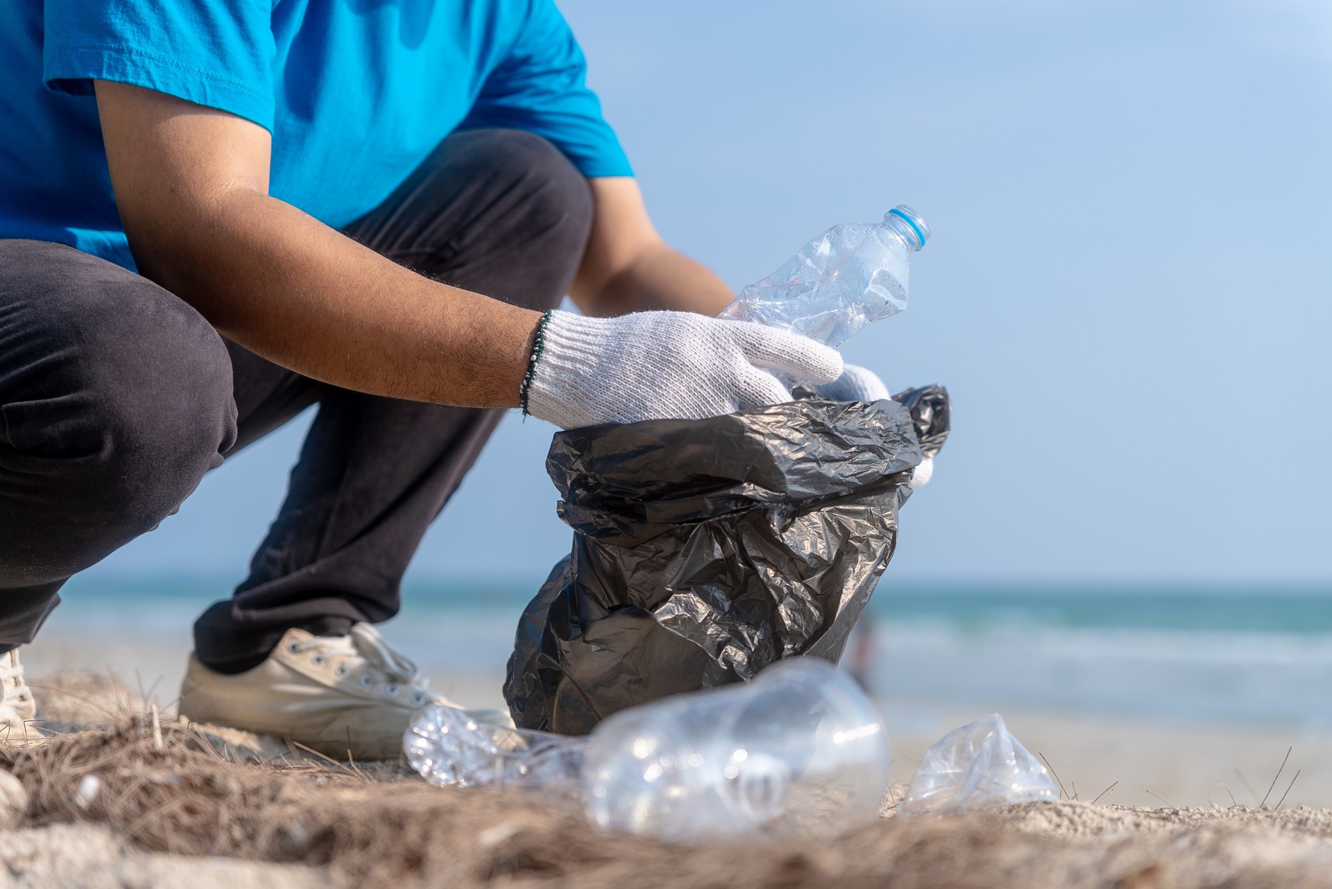 Plastic pollution and environmental problem concept. Happy asian diverse group of volunteers with garbage bags wearing blue t-shirt and cleaning plastic on the beach. Volunteers collecting trash.